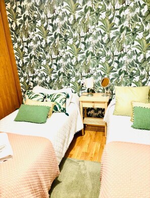 Una habitación con dos camas, una mesita de noche con lámpara y un espejo.