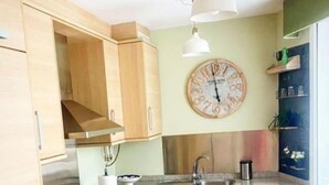 A modern kitchen with wooden cabinets, a granite countertop, a stainless steel range hood, a sink, and a dining area with a table and chairs.