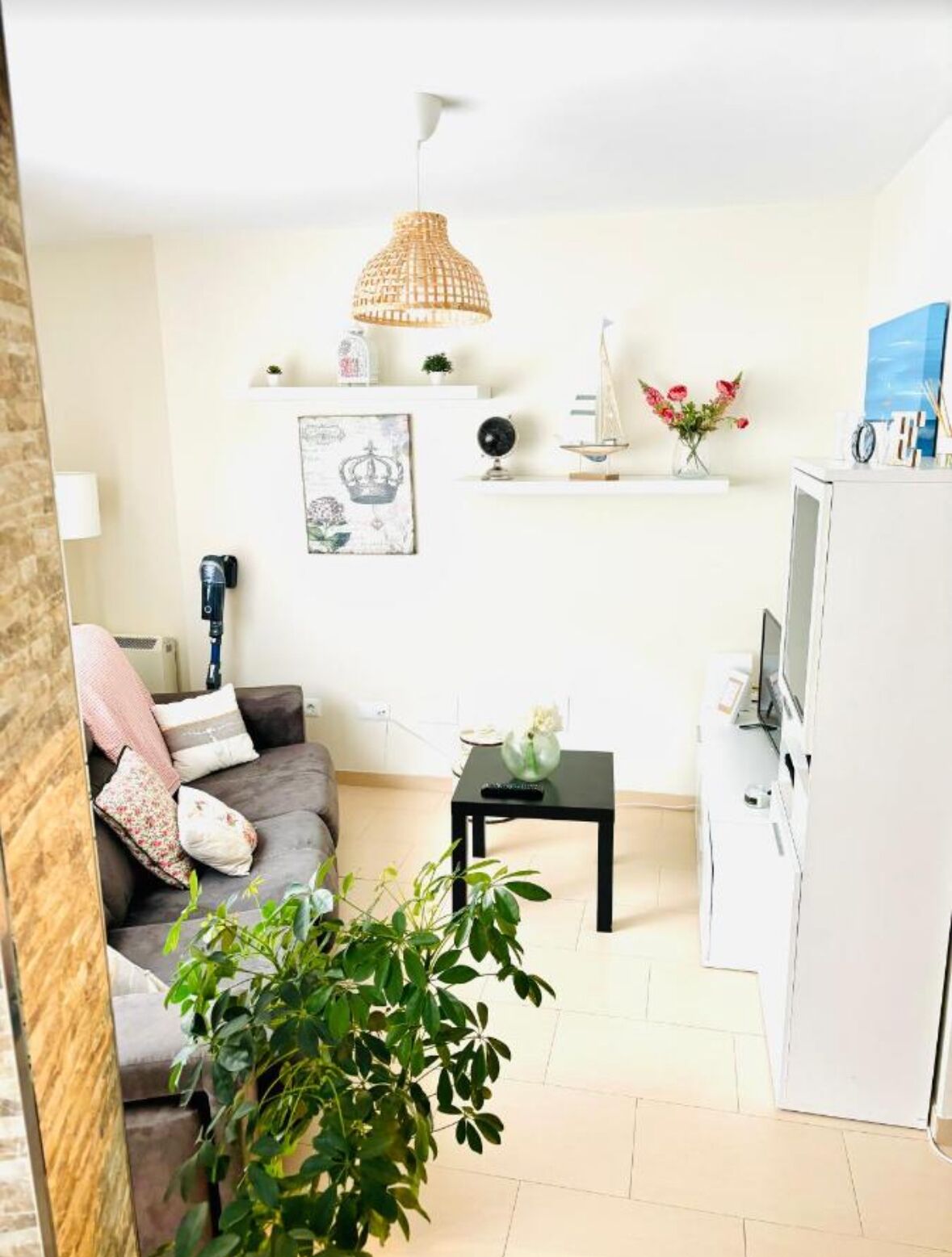 Un salon moderne avec un canapé gris, une petite table basse noire, une plante en pot, un meuble blanc et un luminaire suspendu.