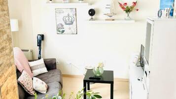 Un salon moderne avec un canapé gris, une petite table basse noire, une plante en pot, un meuble blanc et un luminaire suspendu.