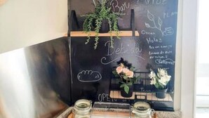 A chalkboard wall with various sections labeled for coffee, tea, and other beverages, along with a small plant and flowers.