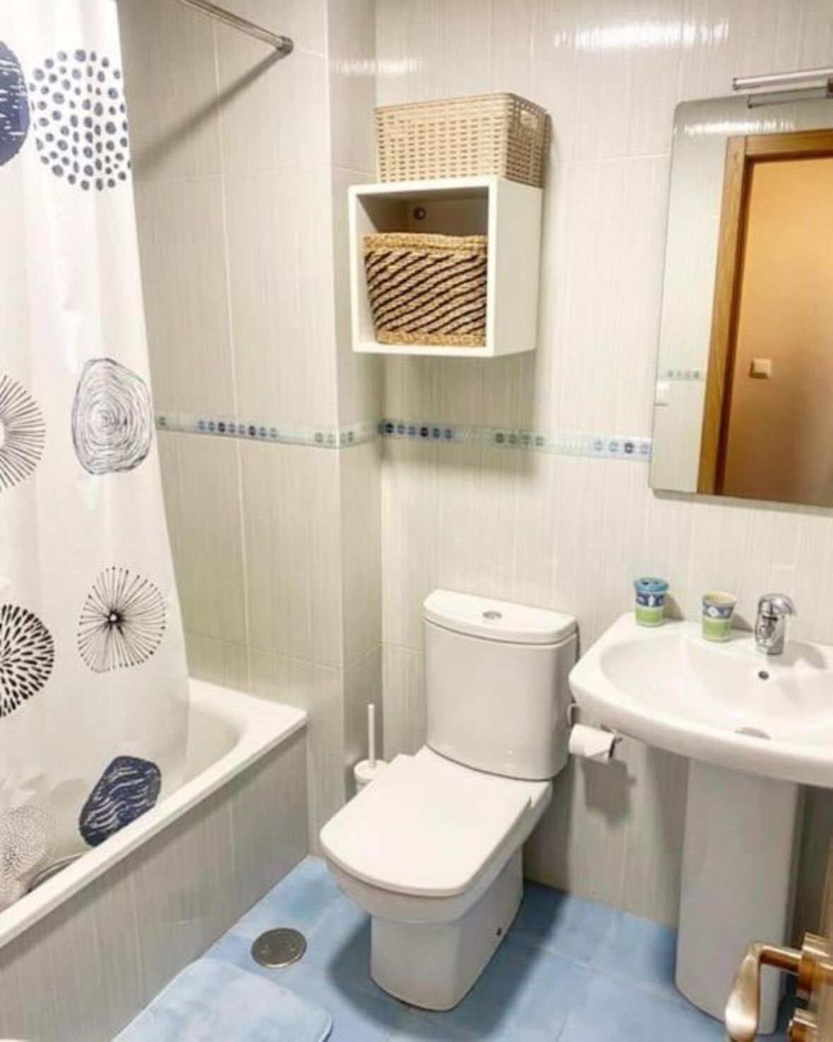 Un baño pequeño con inodoro, lavamanos y estante sobre el inodoro.