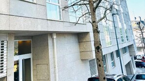 A multi-story building with a modern architectural style, featuring large windows and a tree in front.