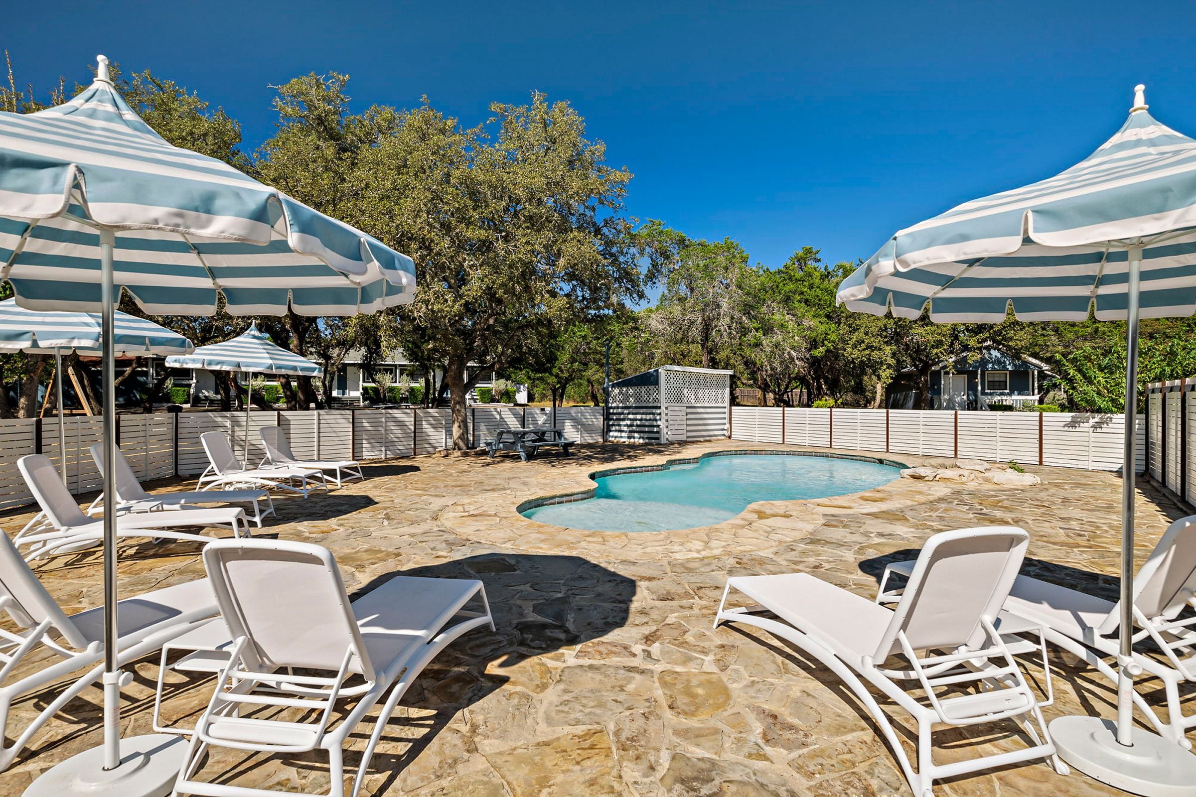 A pool area with stone flooring, white lounge chairs, and striped umbrellas.