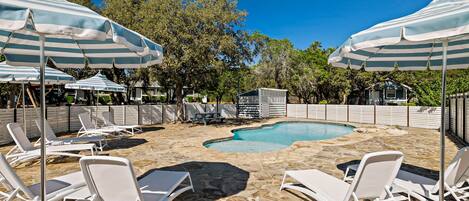 A pool area with stone flooring, white lounge chairs, and striped umbrellas.