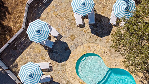 An aerial view of a swimming pool area with stone flooring, surrounded by lounge chairs and striped umbrellas.