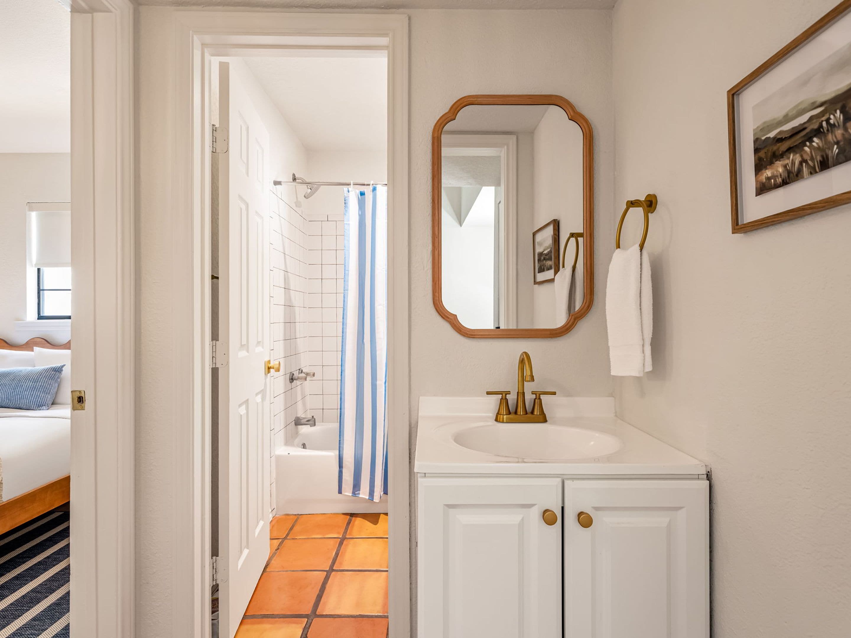 A bathroom with a white sink, gold faucet, and a mirror with a wooden frame.