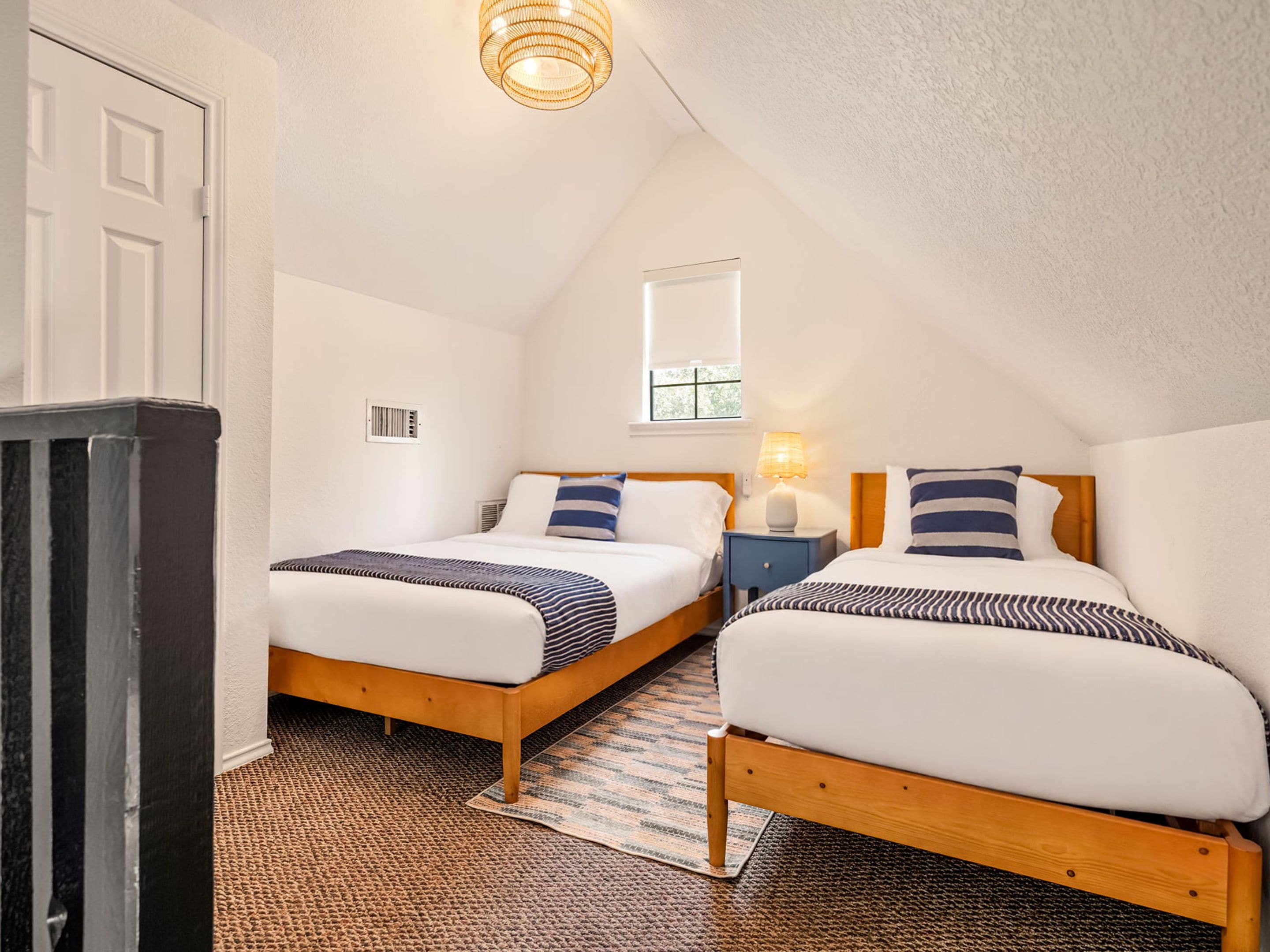 Une chambre avec deux lits, une fenêtre, un luminaire au plafond et une porte.