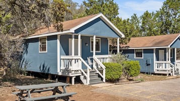A small, single-story cabin with a porch, a picnic table, and a clear view of the surrounding forest.