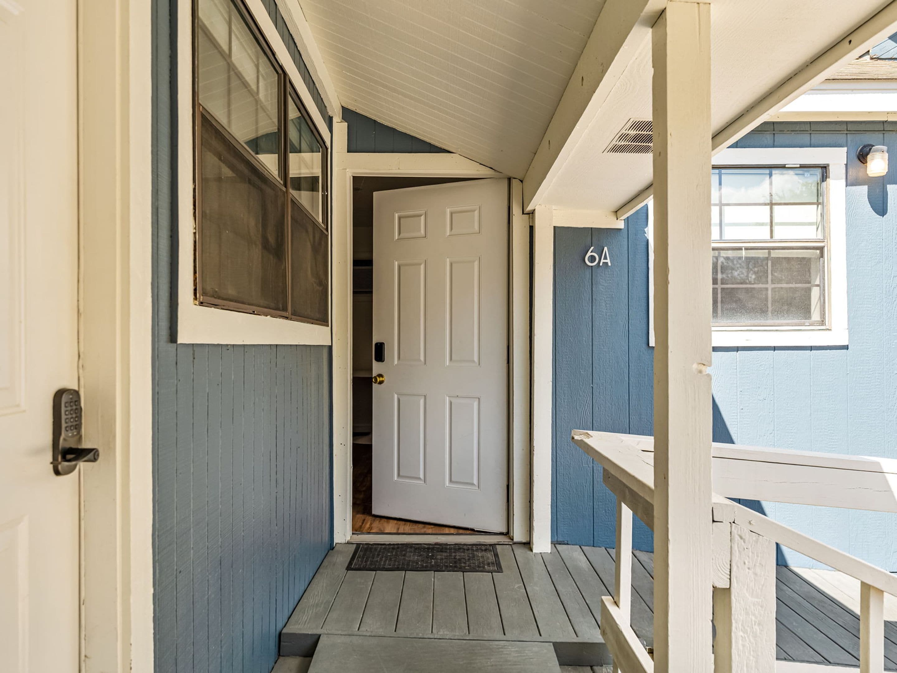 A narrow wooden porch leading to a white door with a number '6A' above it.