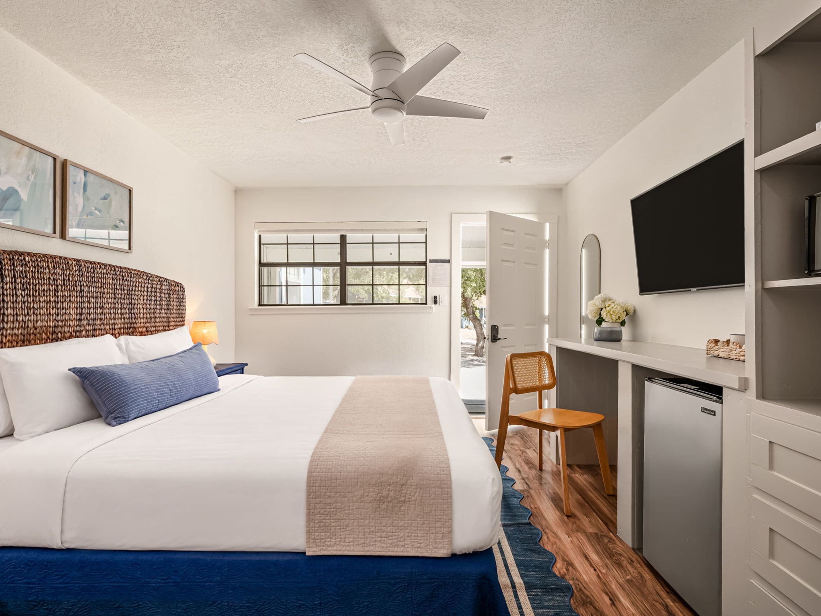 A bedroom with a bed, a desk, a chair, a television, and a ceiling fan.