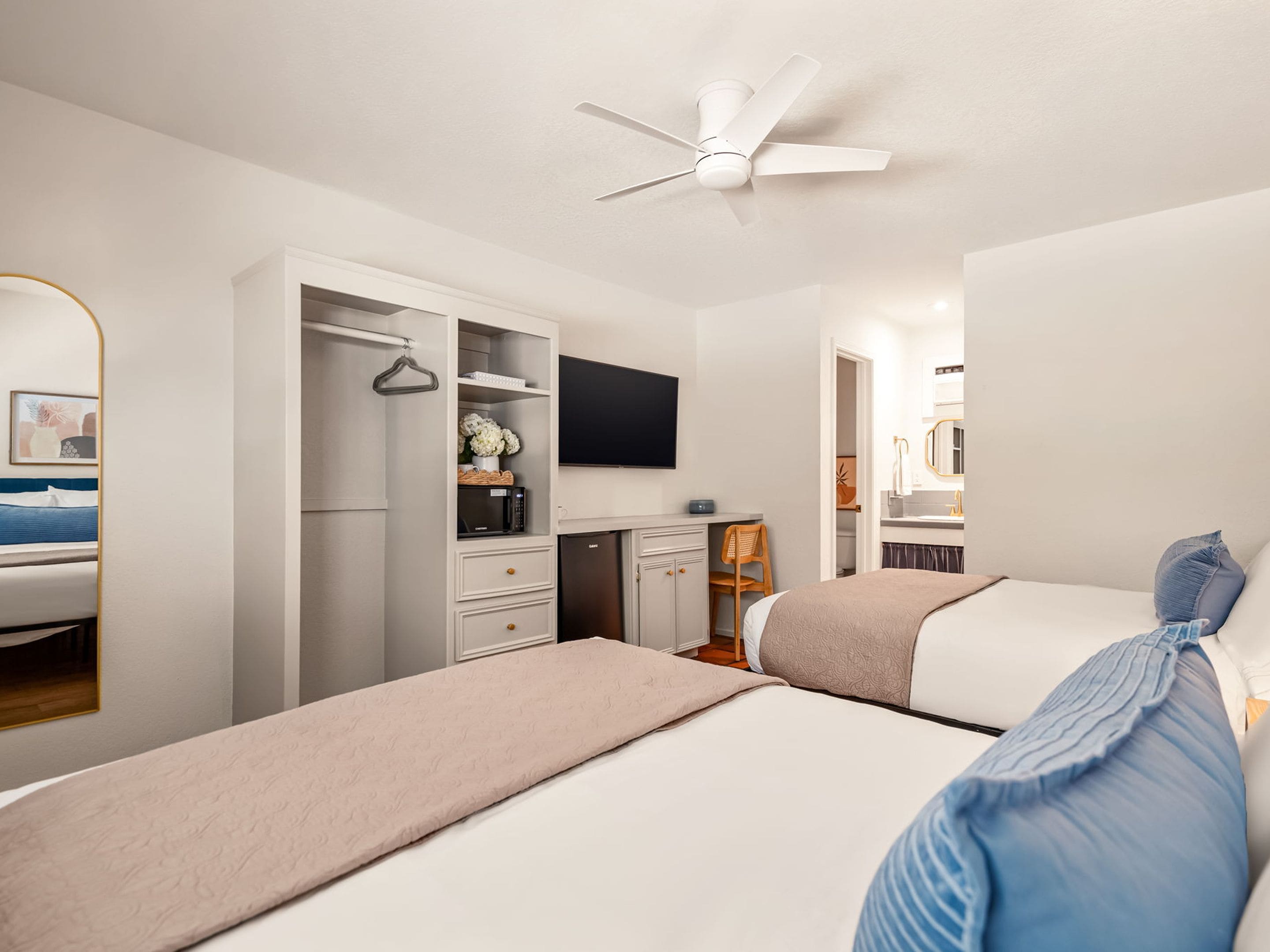 A hotel room with a bed, a wardrobe, a desk, a chair, a television, and a ceiling fan.