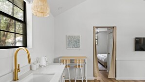 A modern kitchen with a white countertop, gold faucet, and a hanging light fixture.