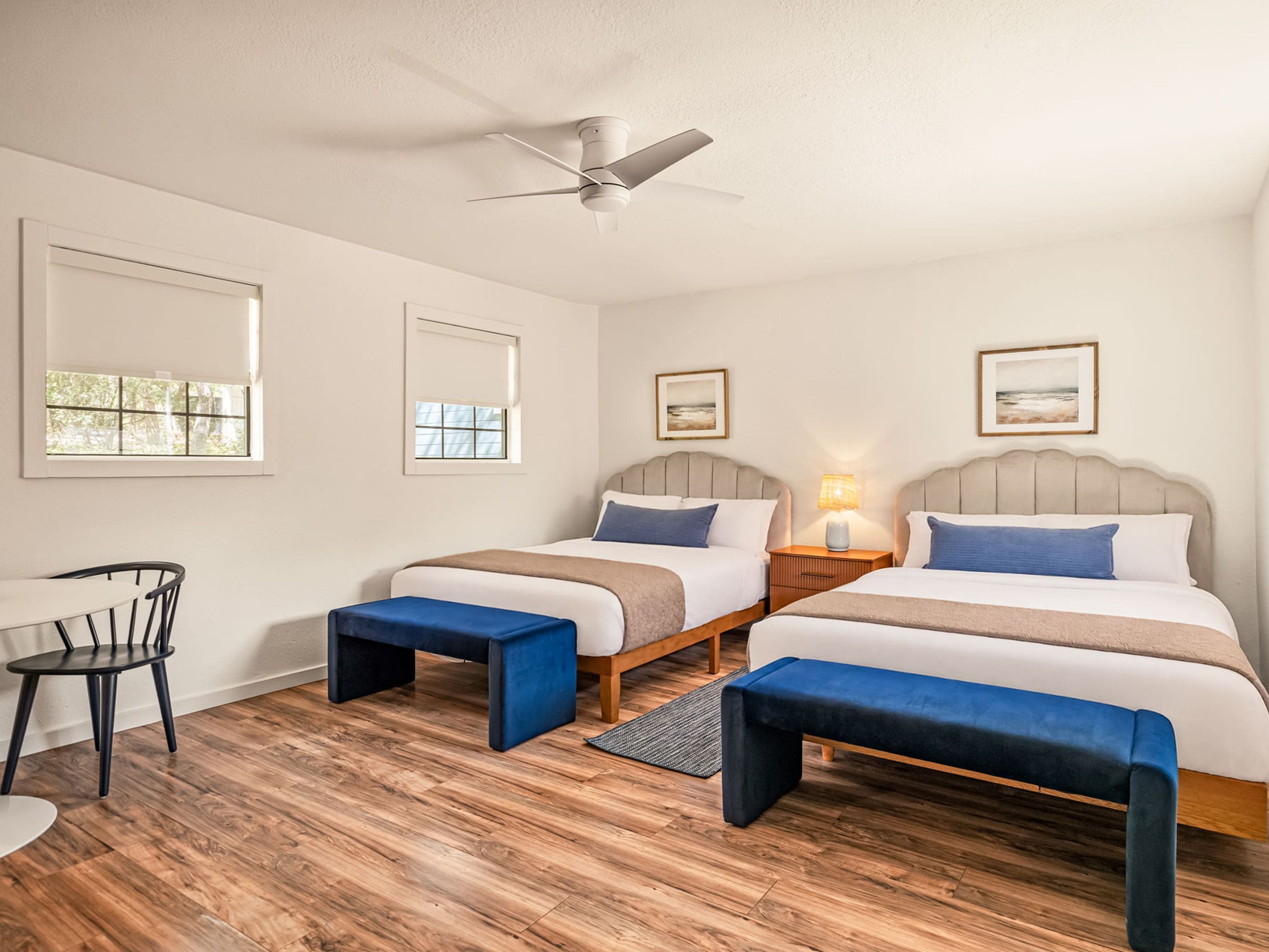 A hotel room with two beds, a ceiling fan, a desk with a chair, and a window.