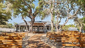 A covered outdoor seating area with wooden benches and a pathway leading to a building with a blue roof.