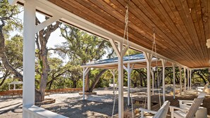 A covered outdoor area with wooden benches and swings, surrounded by trees.