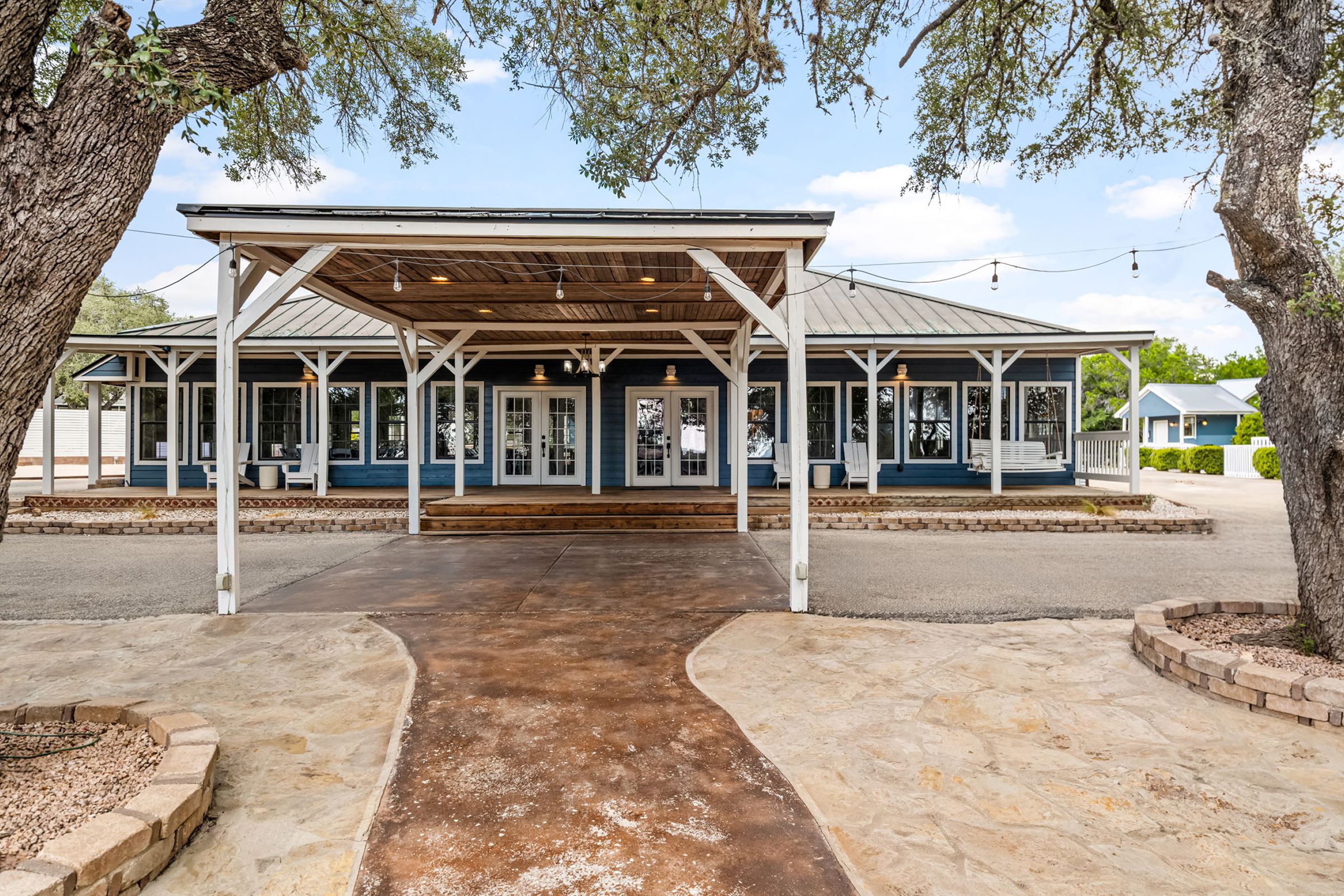 A covered outdoor area with a concrete pathway leading to a building with multiple doors and windows.