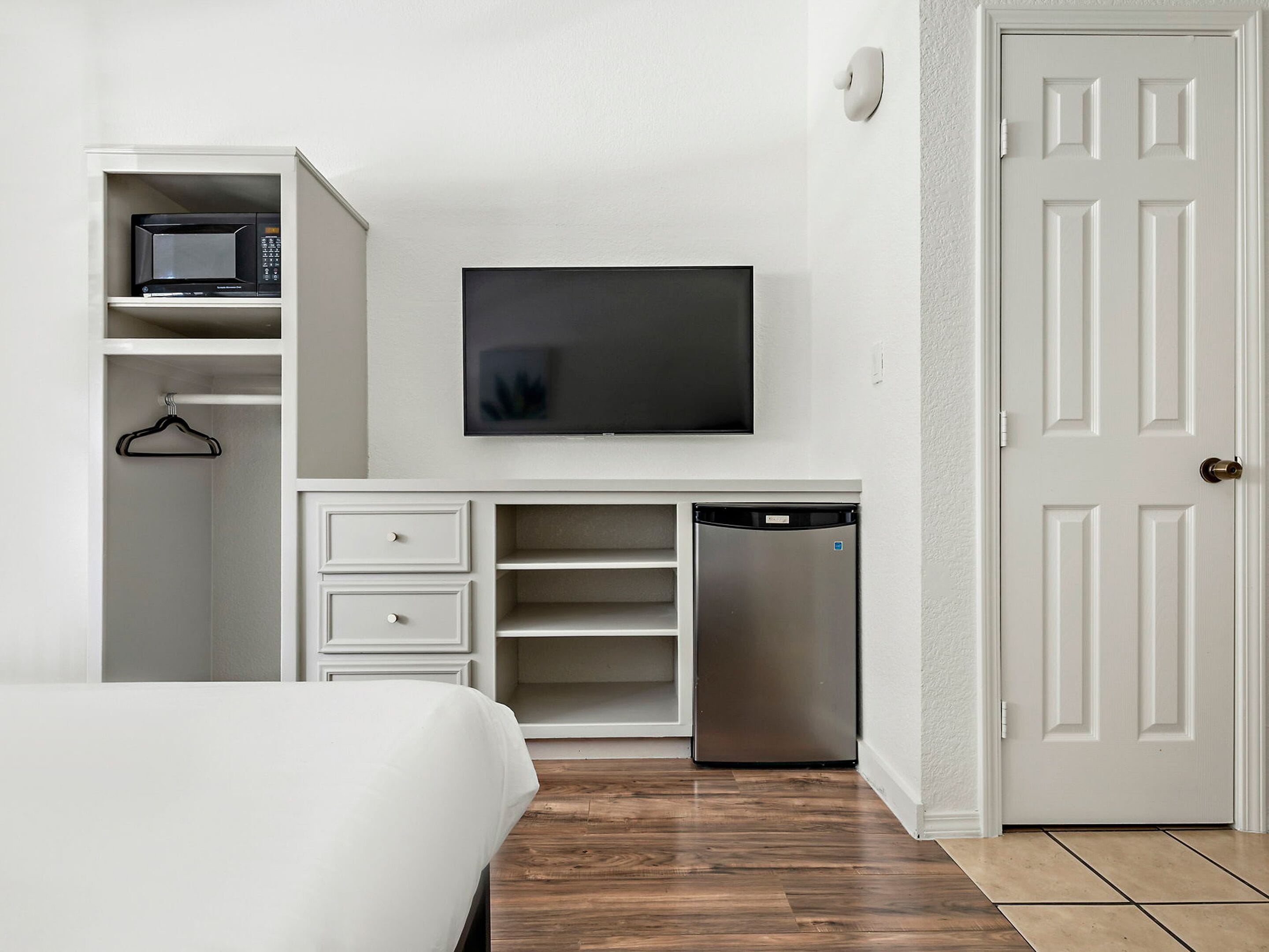 Una camera spaziosa con un letto, un armadio bianco, un forno a microonde, una TV e una lavastoviglie.