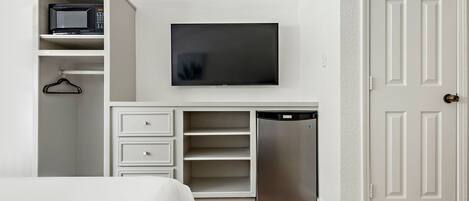 Una habitación compacta con cama, armario blanco, microondas, televisión y lavavajillas.