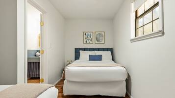 A bedroom with a bed, a nightstand, a lamp, and a window.