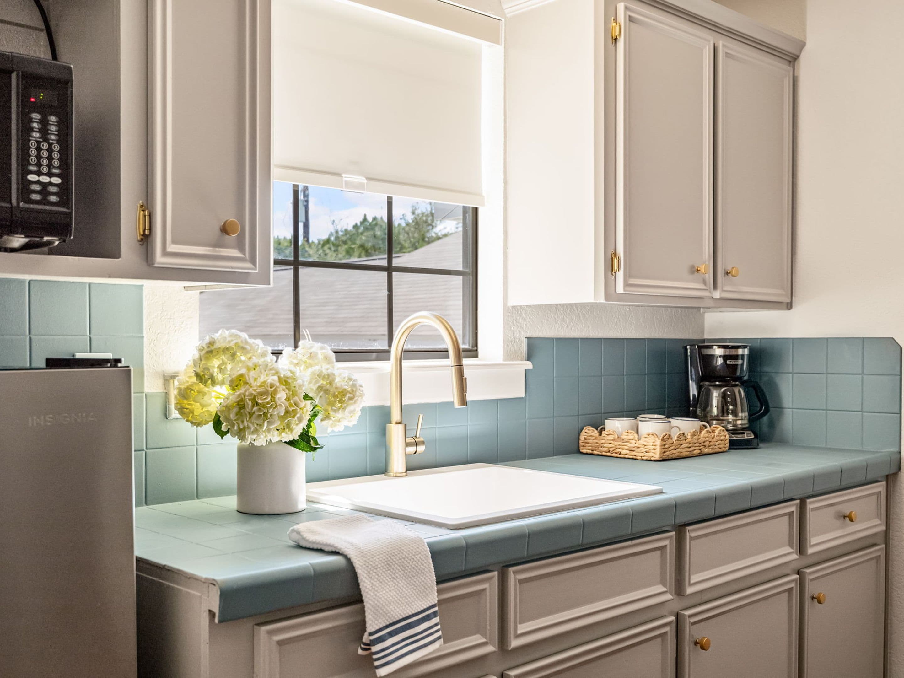 A kitchen with a white sink, a coffee maker, and a vase of flowers on the counter.