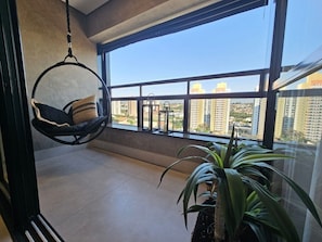 A balcony with a hanging chair, a potted plant, and a view of high-rise buildings.