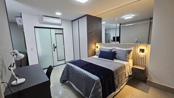 Quarto moderno com cama, mesas de cabeceira, escrivaninha com cadeira e espelho.