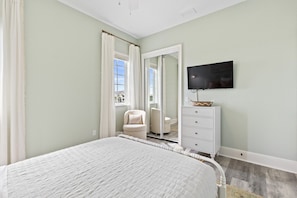 Une chambre à coucher comprenant un lit, une commode, une chaise, un téléviseur et un miroir.