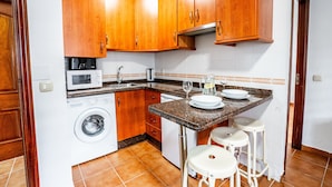 Una cocina compacta con armarios de madera, lavadora, microondas y una pequeña barra con taburetes.