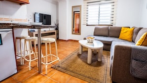 Un espacio habitable compacto con cocina, un sofá con cojines, una pequeña mesa redonda y un taburete.