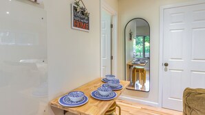 Un comedor con una mesa de madera dispuesta con platos azules y blancos, un espejo en la pared y una puerta a la derecha.