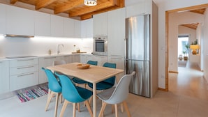 Una cocina moderna con armarios blancos, un refrigerador de acero inoxidable y una mesa de comedor de madera con sillas color verde azulado.