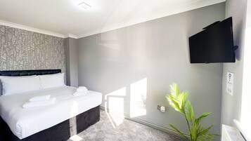 Ein Hotelzimmer mit einem Bett, einem Flachbildfernseher, einer Zimmerpflanze und einem an der Wand montierten Thermostat.