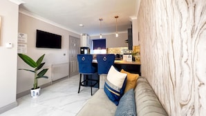 A modern living room with a sofa, a dining area with chairs, a TV mounted on the wall, and a kitchen in the background. - Lock View (Boston)