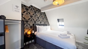 A hotel room with a bed, a nightstand, a lamp, a wall-mounted picture, and a sign indicating free WiFi. - Lock View (Boston)