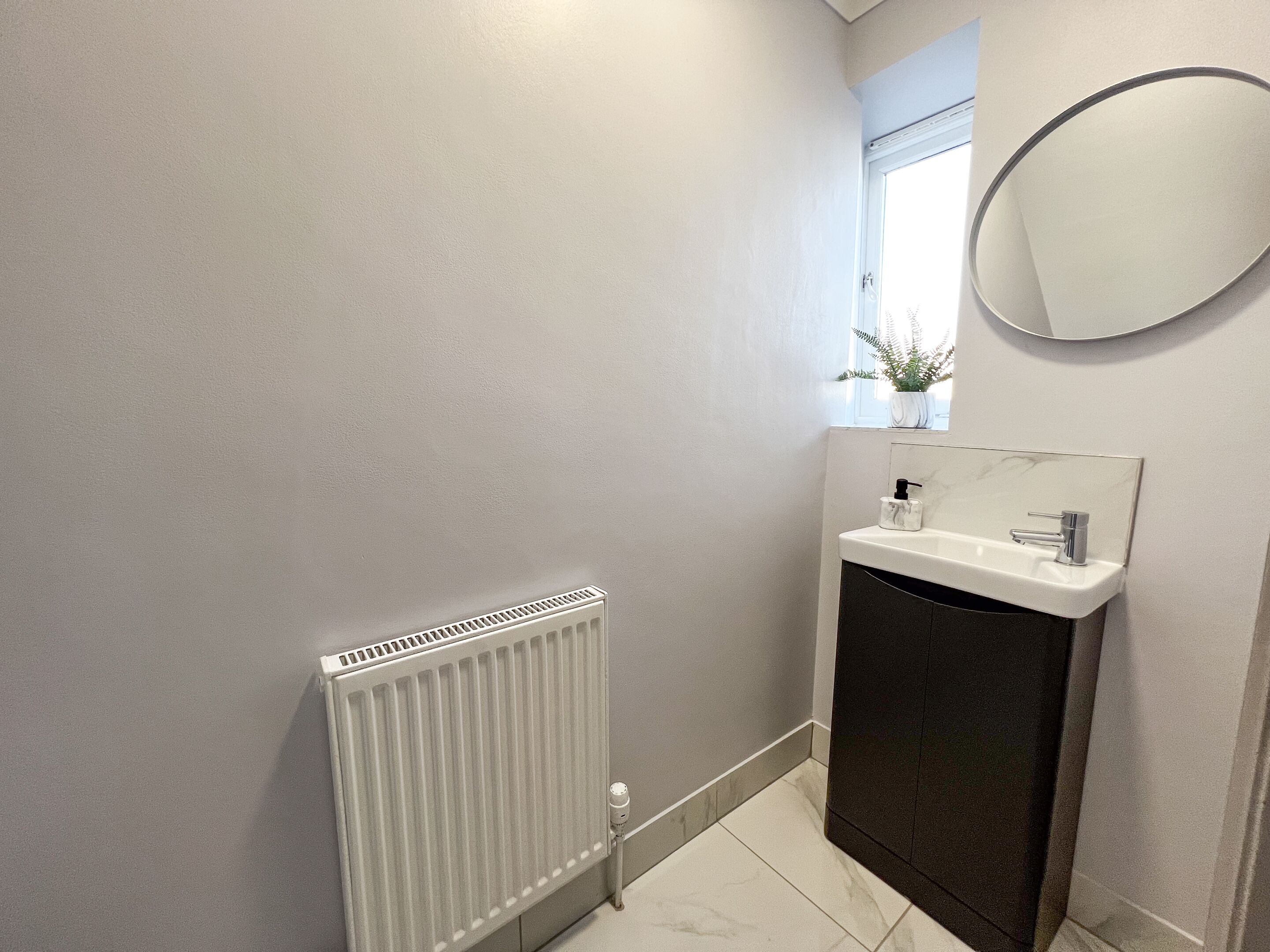 A bathroom with a white radiator, a sink with a marble countertop, and a round mirror.