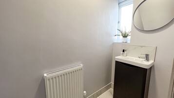 A bathroom with a white radiator, a sink with a marble countertop, and a round mirror.
