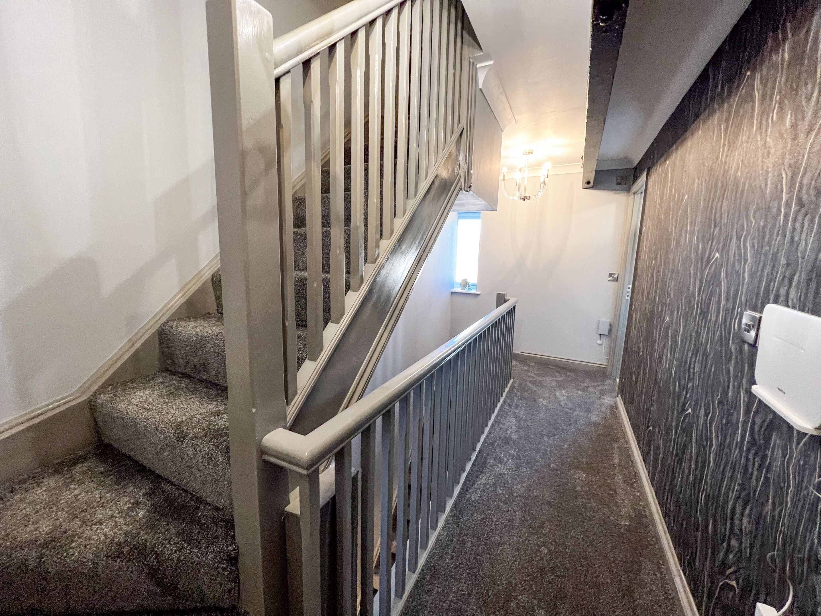 A staircase with a handrail, carpeted steps, and a wall-mounted light fixture.