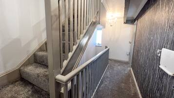 A staircase with a handrail, carpeted steps, and a wall-mounted light fixture.