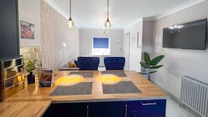 A modern kitchen with a wooden countertop, two pendant lights, and a dining area with blue chairs. - Lock View (Boston)