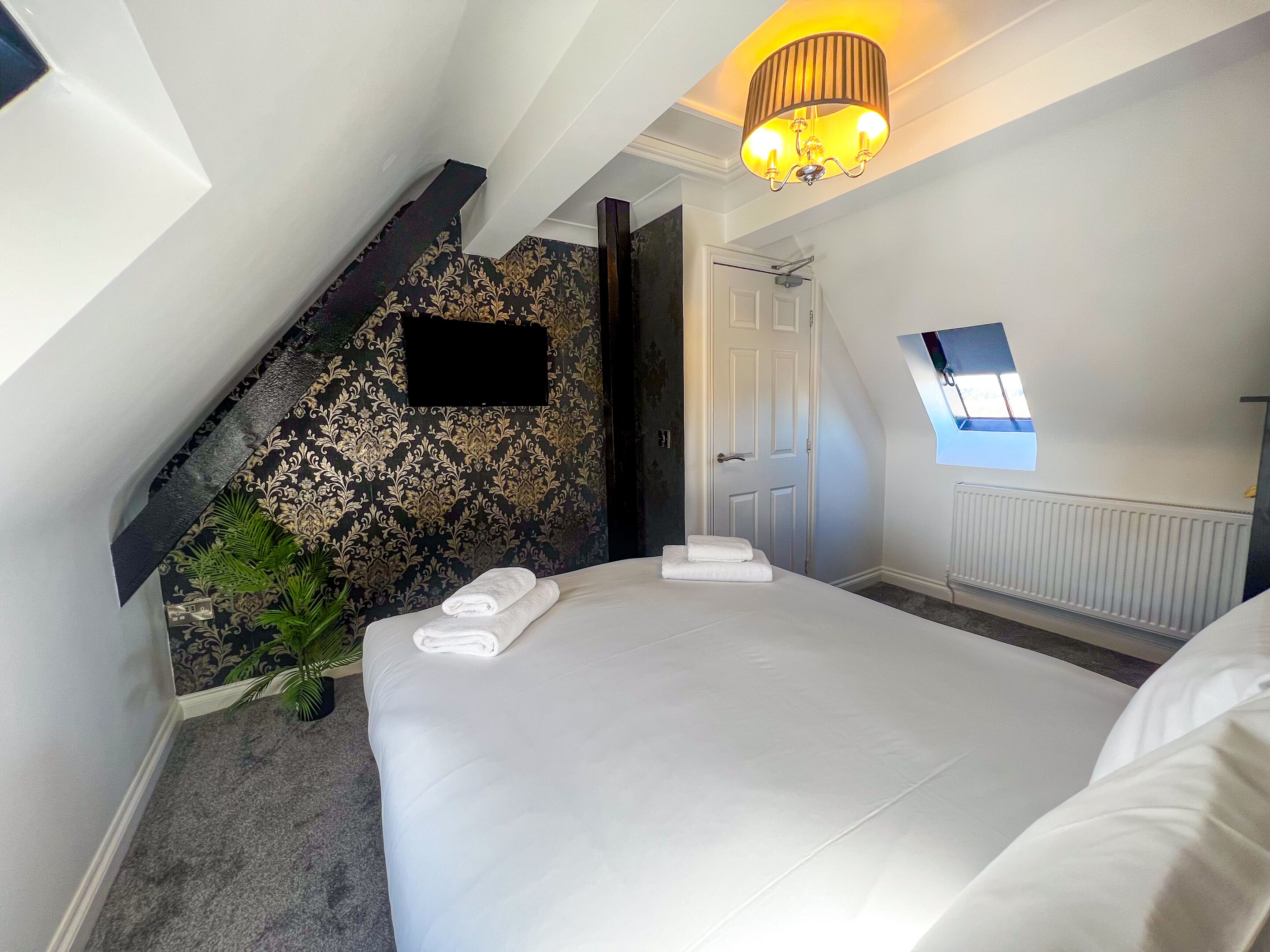 A bedroom with a large bed, a small window, a wall-mounted TV, and a staircase leading to an upper level.