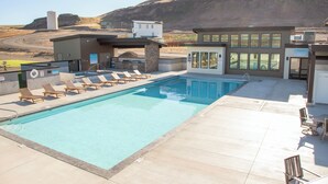 Una piscina amb gandules, un edifici amb grans finestres i una muntanya de fons.