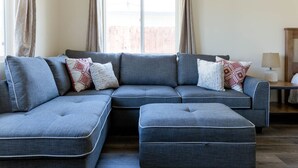Un sofá seccional gris con almohadones estampados, una mesita de madera y una lámpara.