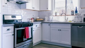 Cocina moderna con armarios blancos, electrodomésticos de acero inoxidable y un ventanal que proporciona luz natural.