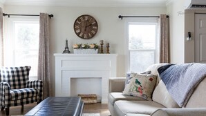 Una sala de estar con chimenea, un reloj y un sillón a cuadros.