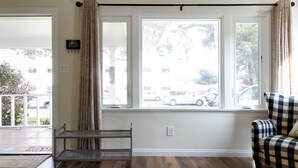 Una habitación con un banco, una silla de cuadros y un ventanal con cortinas.