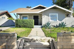 Guests can enter this charming home through the covered porch and front door, surrounded by a well-manicured yard and a wooden fence.
