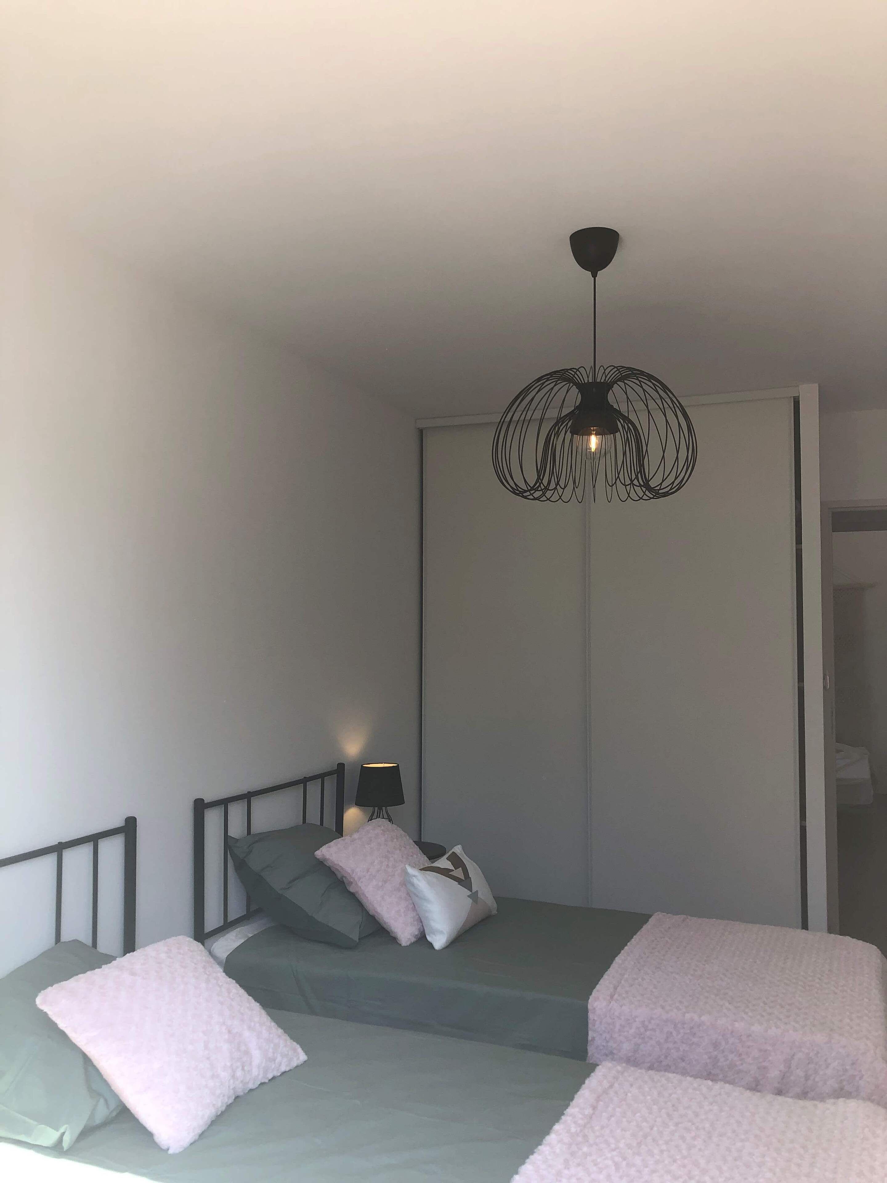 A bedroom with a bed, a bedside table, a lamp, and a hanging light fixture.