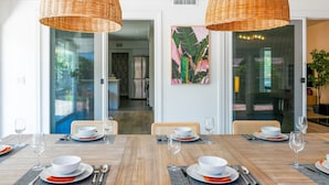 A dining area with a wooden table set for four, surrounded by wicker chairs.