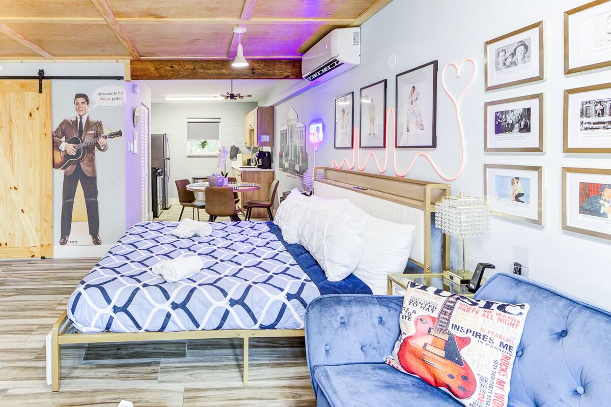 Un dormitorio con una cama, un sofá azul, una puerta de madera y cuadros en la pared.